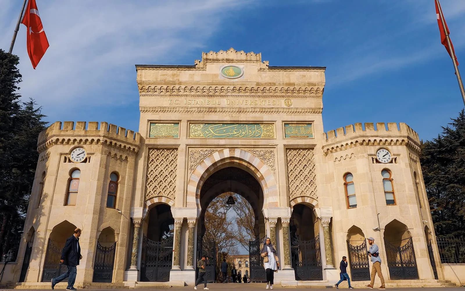 İstanbul Üniversitesi'nin Beyazıt'taki tarihî ana kapısı; iki yanında Türk bayrakları, önünden geçen öğrenciler.